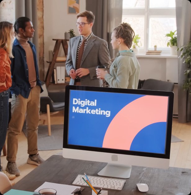 Small team talking beside a desktop computer showing a digital marketing slide