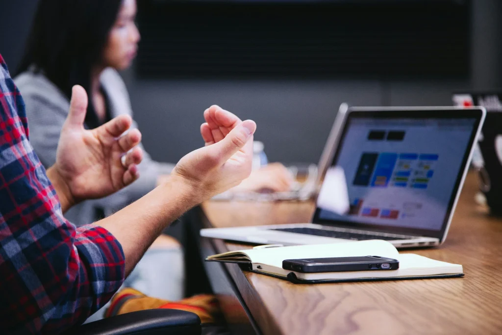 Marketer talking with hands raised beside a laptop, illustrating backlink strategy planning