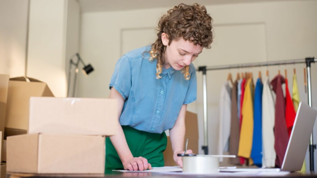 Small business owner packing orders at a laptop beside clothing racks, illustrating how to grow online sales