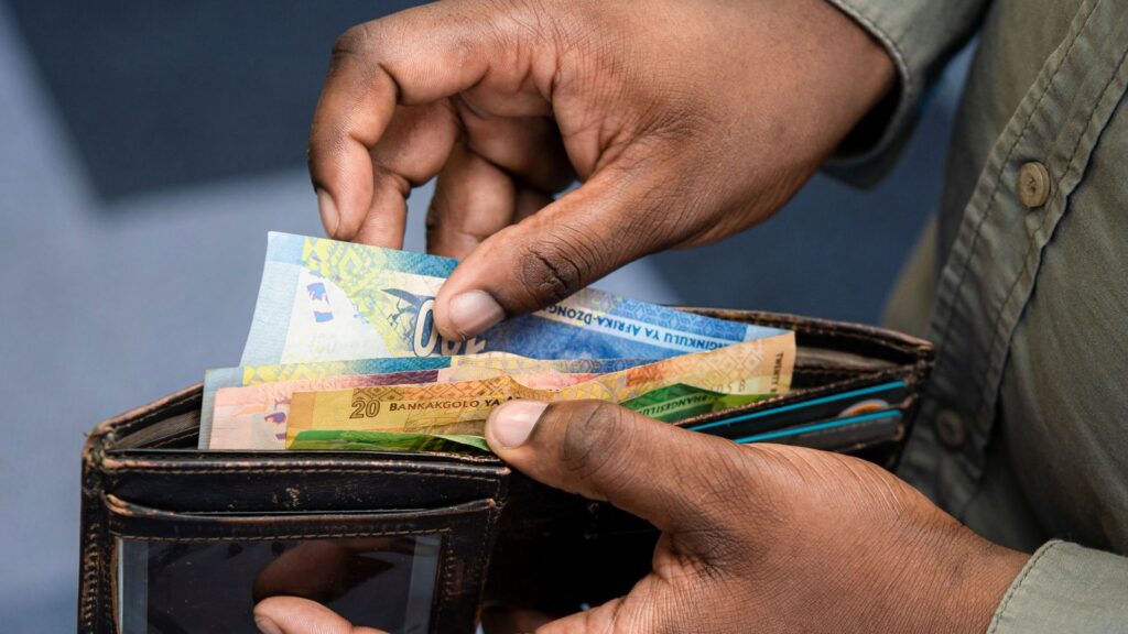 Hands taking cash out of a wallet, illustrating where household spending goes when budgets tighten